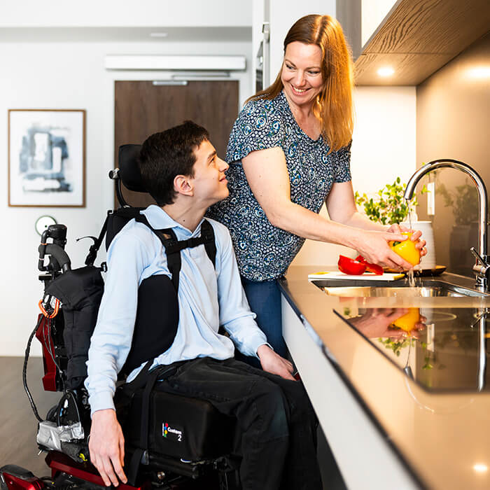 Building Beyond Barriers-Impact Report Cover. Man in a Wheelchair talking to a woman washing fruit in the kitchen sink.