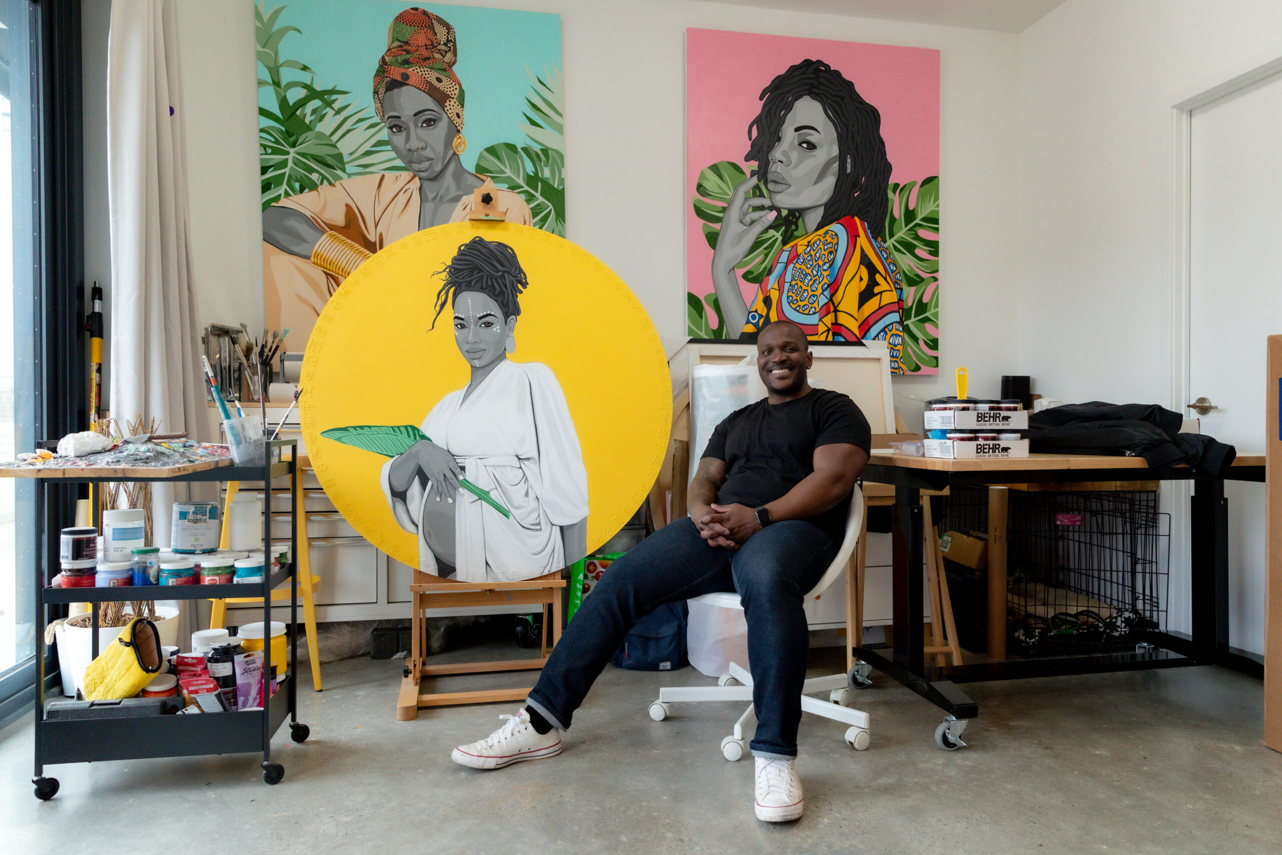 Artist Benny Bing sitting in front of colourful canvas inside his studio in Regent Park