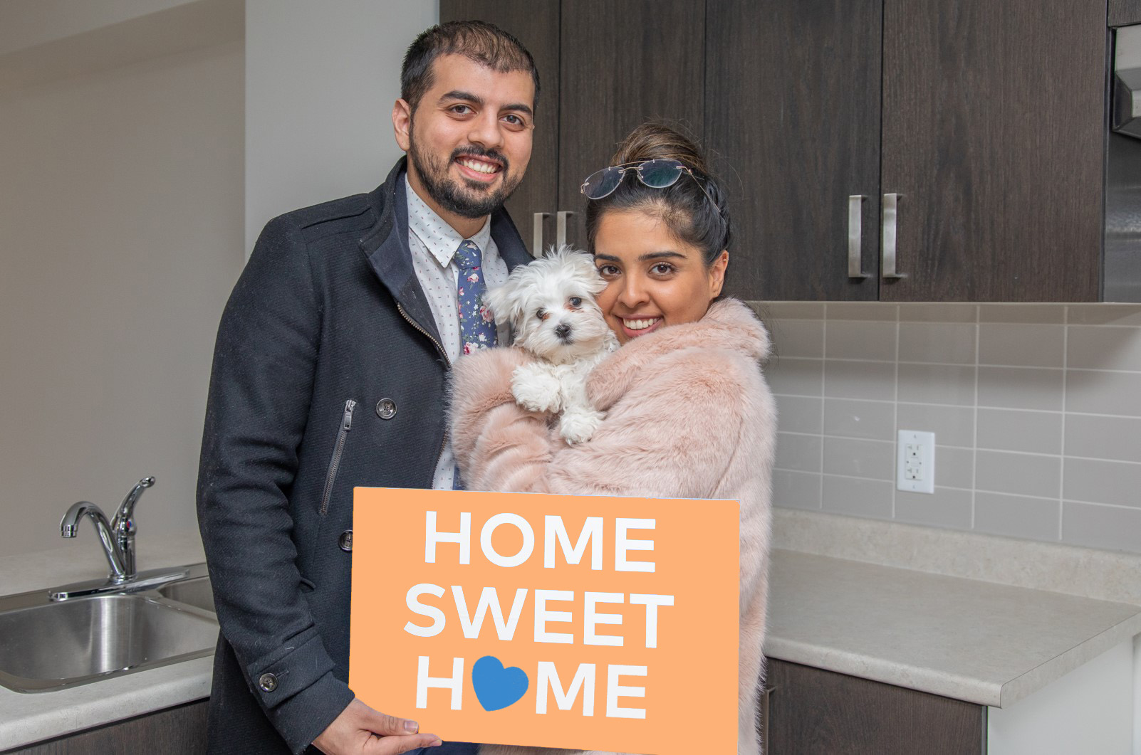 a happy couple with white puppy holding a sign that says home sweet home residents gardening on the rooftop of high rise building in Regent Park